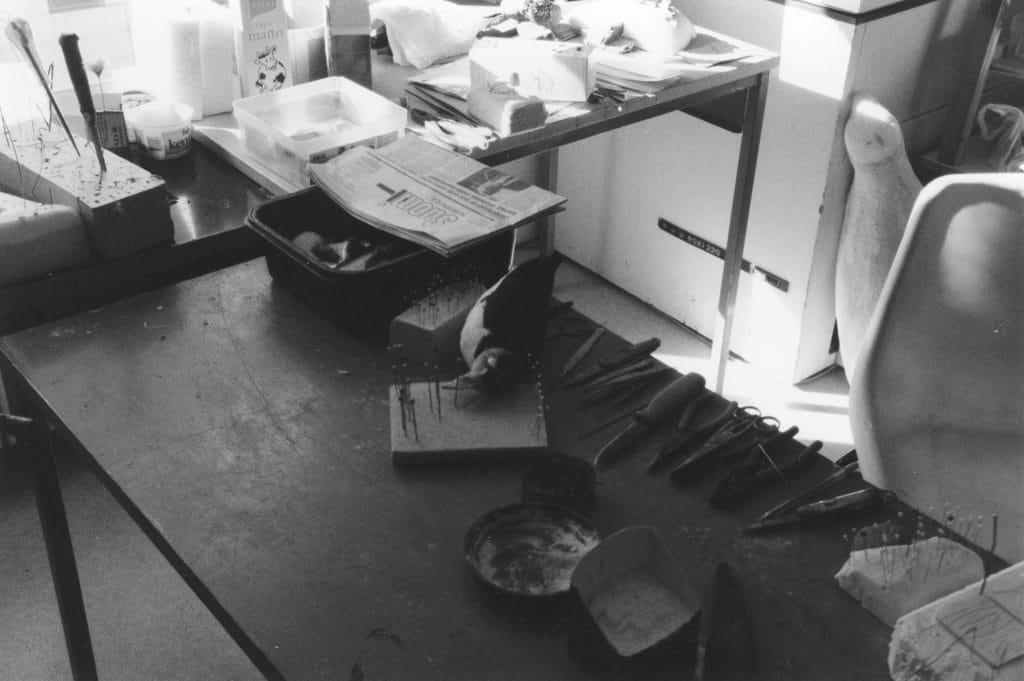 Tweezers, knife, scissors, cutting pliers and tongs on a work table. Among other things there is a puffin on a table as a work in progress.