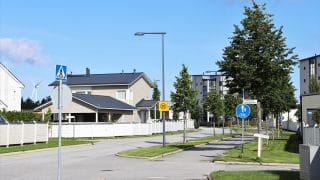 Vy över Havsparkens bostadsområde. I mitten på bilden syns en asfalterad väg samt cykelväg vilka leder till området. Längs dem växer små lövträd. Bakom träden, lyktstolparna och trafikmärken i förgrunden finns egnahemstomter med staket. Längre bort syns också ett våningshus. I bildens vänstra kant, mellan två egnahemshus, syns också ett vindkraftverk längre bort.