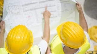 Kypäräpäiset rakentajat tutkivat piirrustuksia