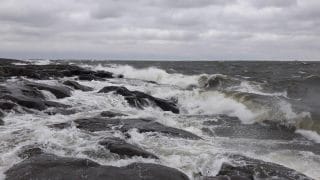 Syksyinen maisema, jossa vaahtopäiset aallot iskevät kallioihin.