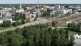 Vy fotad högt snett uppifrån. I förgrunden finns träd och bakom dem syns järnvägsstationens bangård samt bakom den öppnar sig staden med sina byggnader. Långt borta i horisonten syns också Karlebys vattentorn.