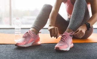 Kuvassa jumppamatto, juomapullo ja nainen sitomassa lenkkarit jalkaan