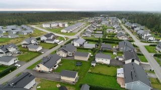 Vy uppifrån över Puntusåsens bostadsområde som främst består av egnahemshus med gröna gårdsplaner. Bakom området breder skogen ut sig och ännu längre bak havet på avstånd.