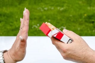 Naisen käsi on torjuvasti pystyssä miehen käden tarjoamaa tupakka-askia kohden.