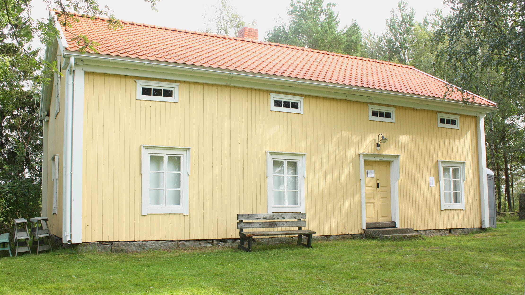 Keltainen vanha puurakennus kuvattuna kesäpäivänä.