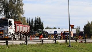 Byggandet av Halkokari cirkulationsplats på sommaren. I vänstra kanten står en lastbil parkerad vid vägkanten och bakom den arbetsplatsområdet med arbetare och utrustning som behövs för arbetet.