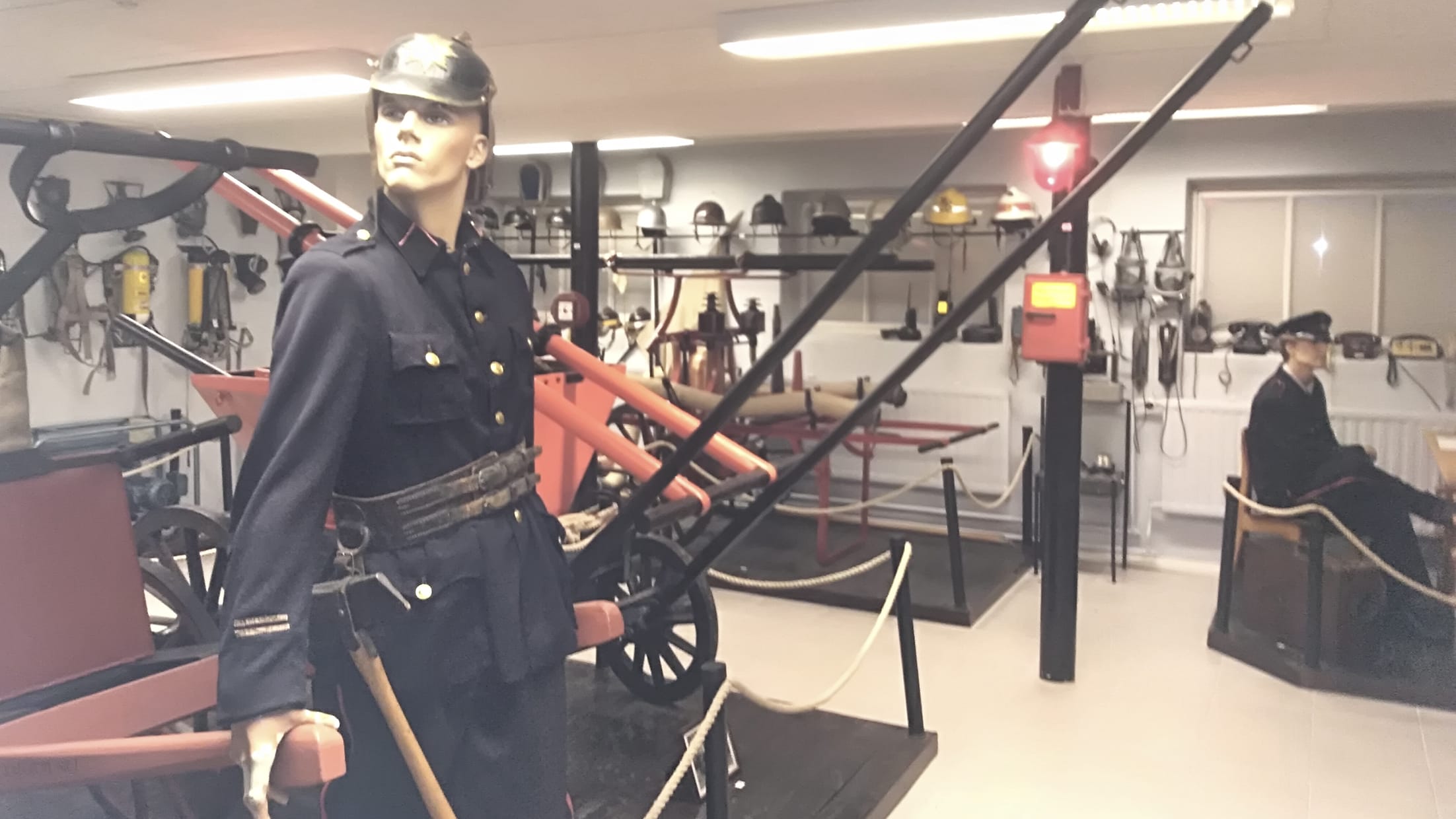 Interiööri, jossa vanhoja palotarvikkeita ja palomiehiksi puettuja mallinukkeja.