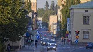 Katunäkymä Torikadulta. Kadun molemmin puolin on korkeita rakennuksia ja kadulla paljon autoja sekä pyöräilijöitä.