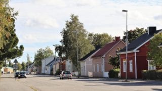 Katunäkymä Kustaa Aadolfinkadulta. Kuvan etualalla kulkee kaksisuuntainen tie, jossa kulkee useita autoja. Kuvan oikeassa reunassa, tien takana näkyy monenvärisiä rintamamiestaloja ja niiden pihoissa kasvavia lehtipuita.