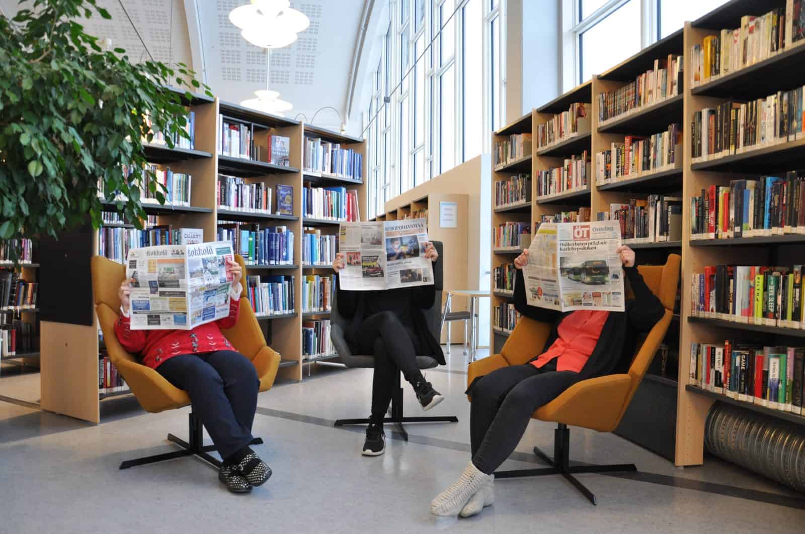 Lehdenlukijoita kirjaston hyllyjen edessä.