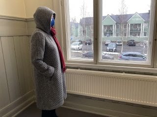 Naisen yllä hupullinen mustavalkoinen villakangastakki, huppu nostettuna ylös.