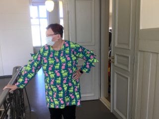 Nainen esittelee koirakuvioista trikoopuseroa, jossa hihoissa kolmiokoristelu.