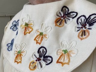 Yksityiskohta kauluksesta, jossa kirjailtuja orvokkeja.