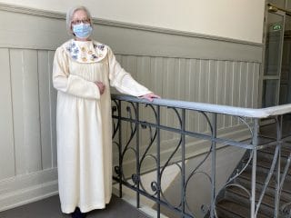 Nainen valkoisessa, käsinkirjaillussa pitkässä puvussa.