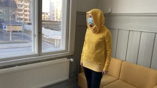 Nainen esittelee keltaista trikoohupparia.