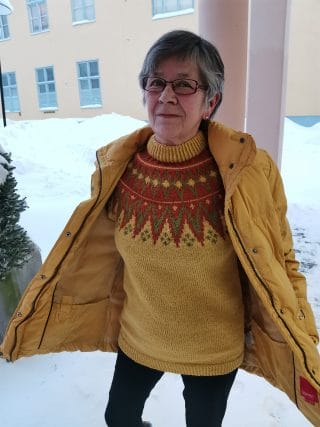 Nainen esittelee neulomaansa keltaista villapaitaa.