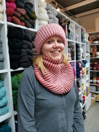 Naisella yllään vaaleanpunaisesta langasta itseneulomansa pipo ja kauluri.