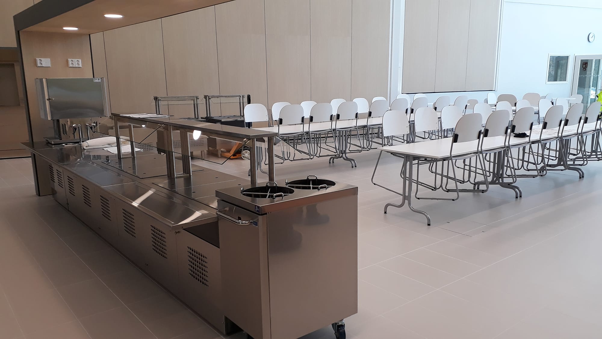 Ykspihlajan koulun tyhjillään oleva ruokala. Etualalla ruokalinjasto ja sen takana kaksi pitkää ruokapöytää ylös nostettuine tuoleineen.