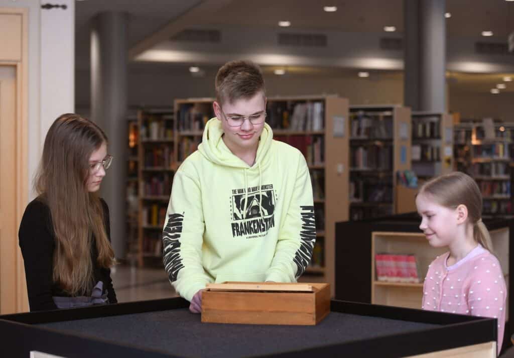 Three kids stand around a table playing a game of Labyrinth.