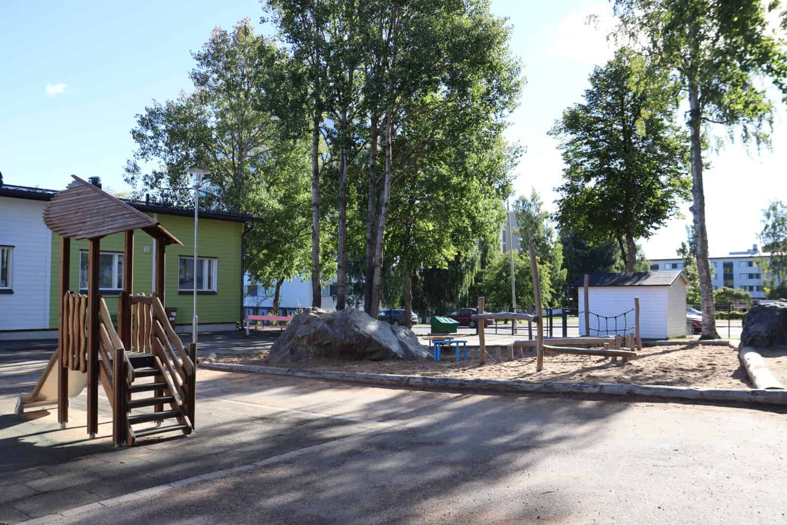 Päiväkotipiha, jolla puita, leikkivälineitä ja kiipeilyteline