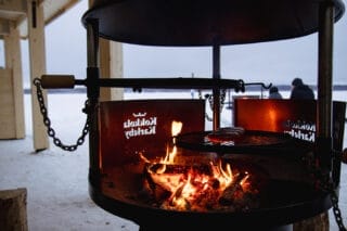 Närbild av en grillplats där en brasa brinner. Landskapet är vintrigt.