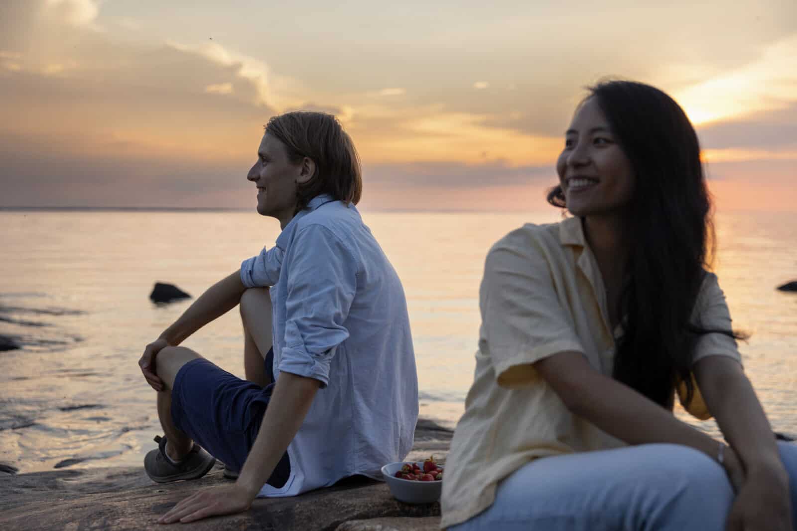 Kvinnan och mannen sitter vid havet. Kvälsolen färgar havet guld