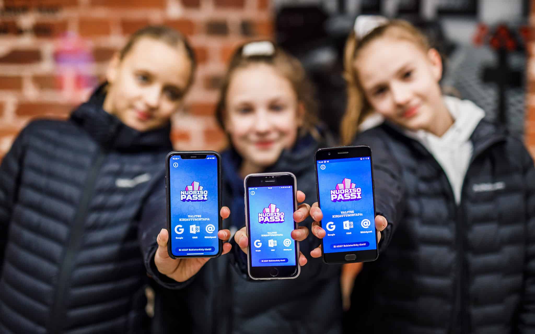 Kolme nuorta näyttää Nuorisopassi-sovellusta puhelimeltaan
