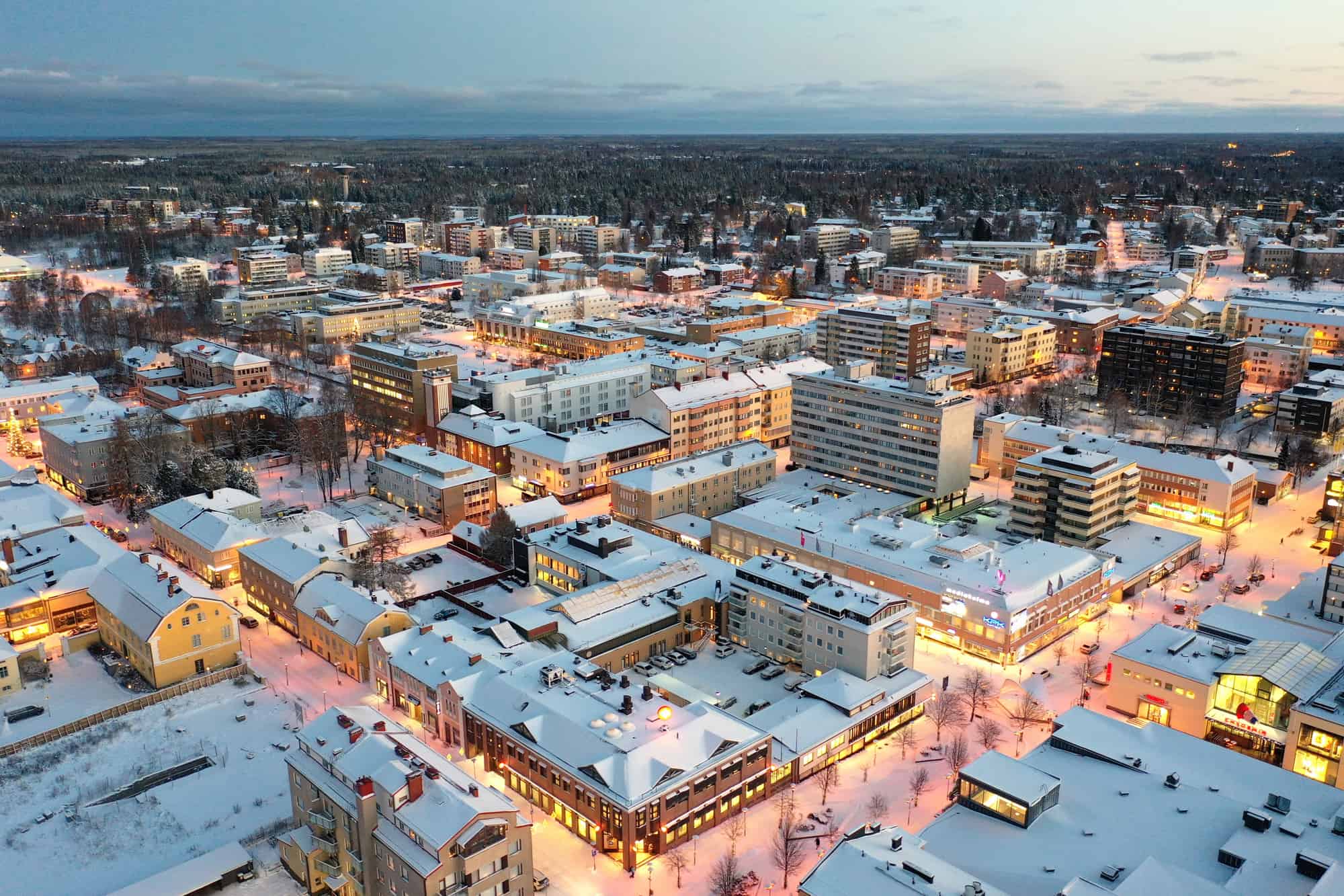 Talvinen ilmakuva Kokkolan keskustasta. RAkennuksien katoilla lunta, katuvalot palavat. Horisontissa siintää metsää ja siniharmaa taivas