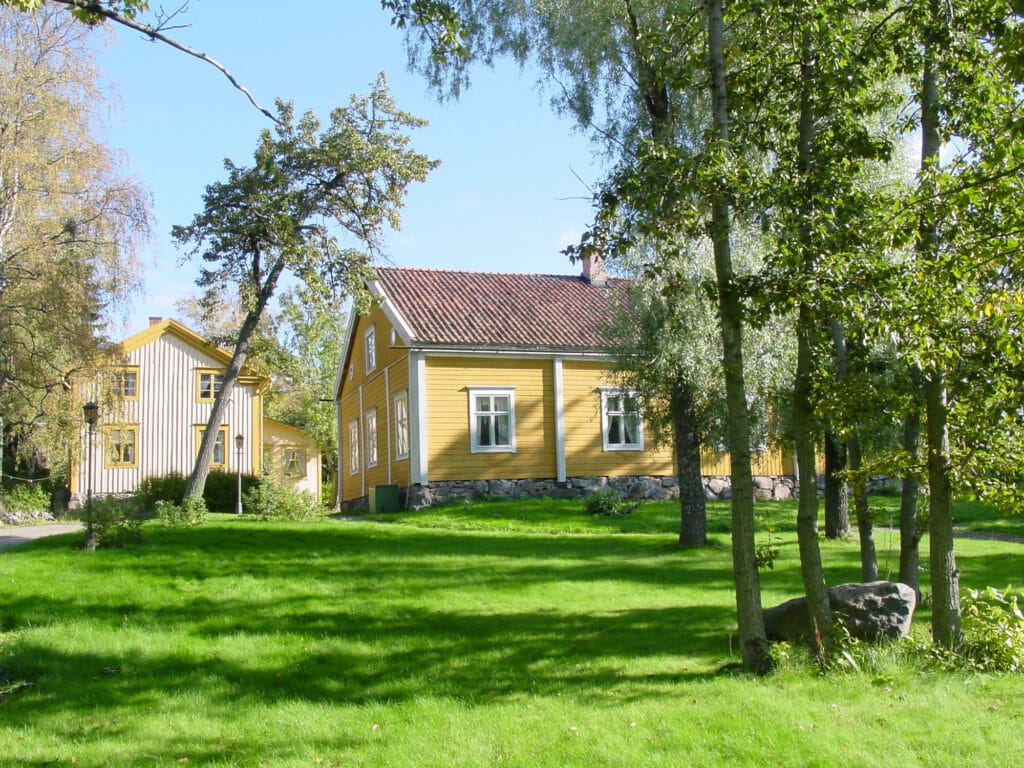 Keltainen puurakennus näkyy nurmialueen ja puiden takana