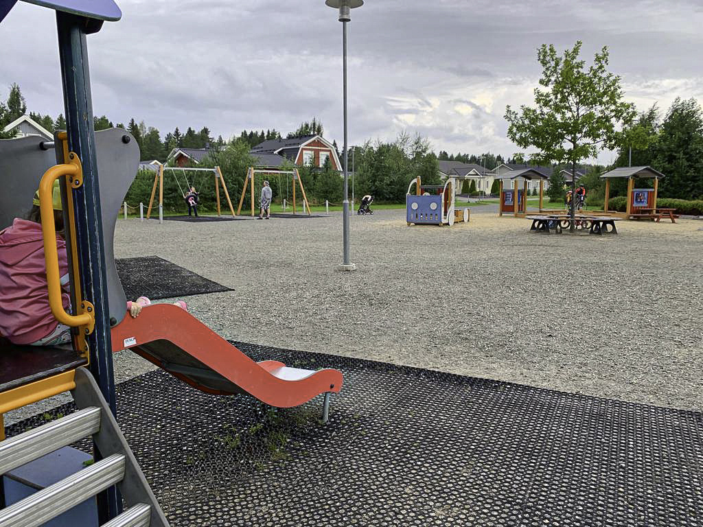 Leikkipuisto, etualalla liukumäki, taustalla keinuja ja omakotitaloja