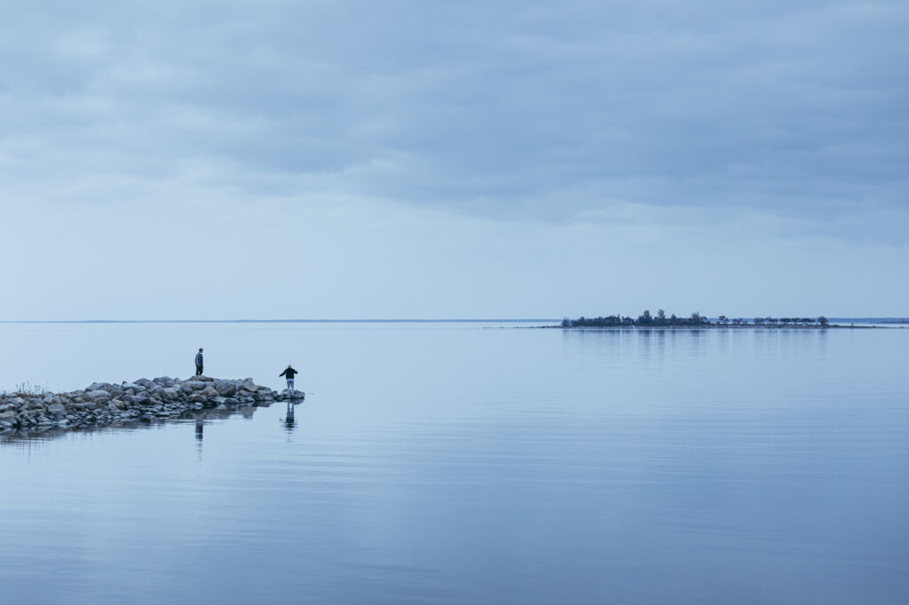 Kaksi ihmistä seisoo kivikoilla meren rannassa.