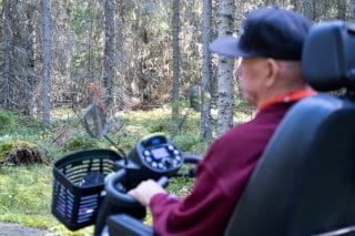 Sähköpyörätuolin käyttäjä kulkee metsässä.