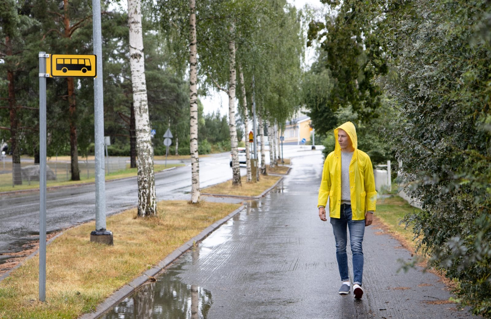Nuori mies keltaisessa sadetakissa kulkee kohti bussipysäkkiä