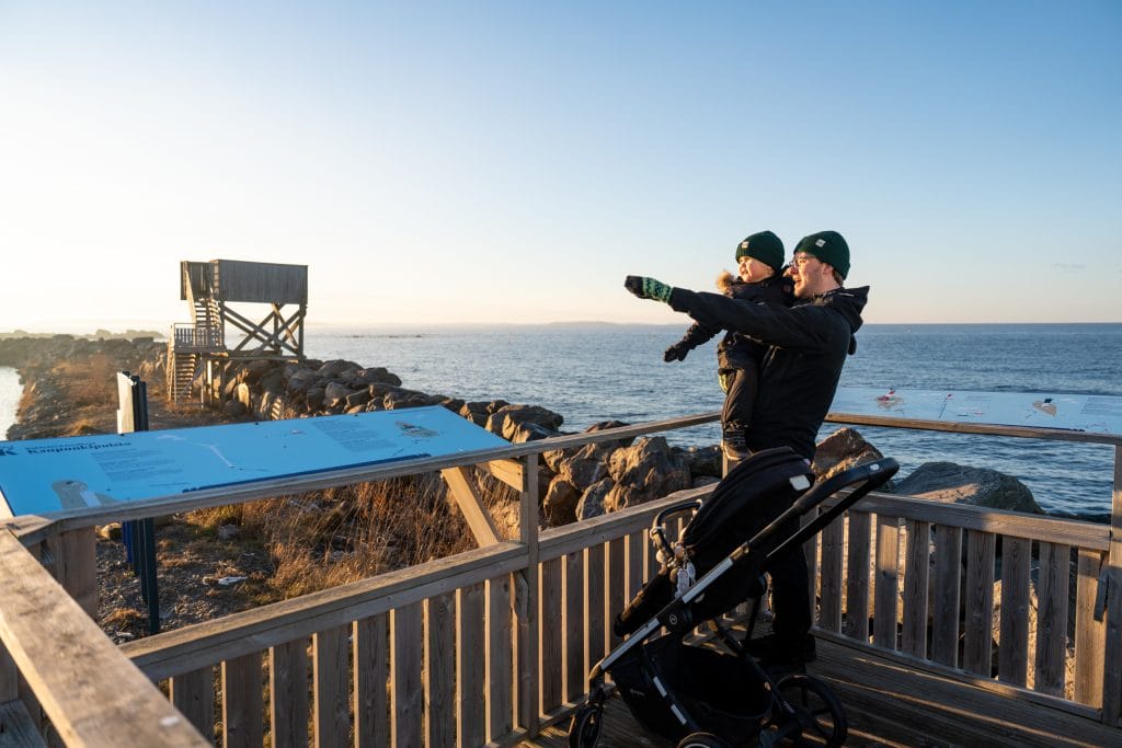 Mies ja lapsi katsovat näkymiä puisessa lintutornissa. Taustalla näkyy toinen lintutorni ja meri.