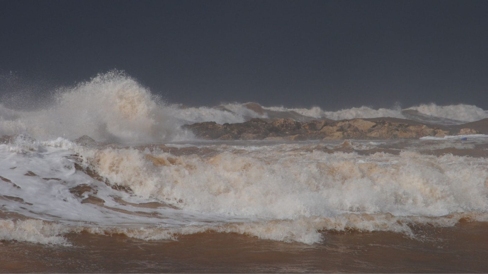 Myrskyävä meri, vaahtopäisiä aaltoja. Taustalla tumma taivas