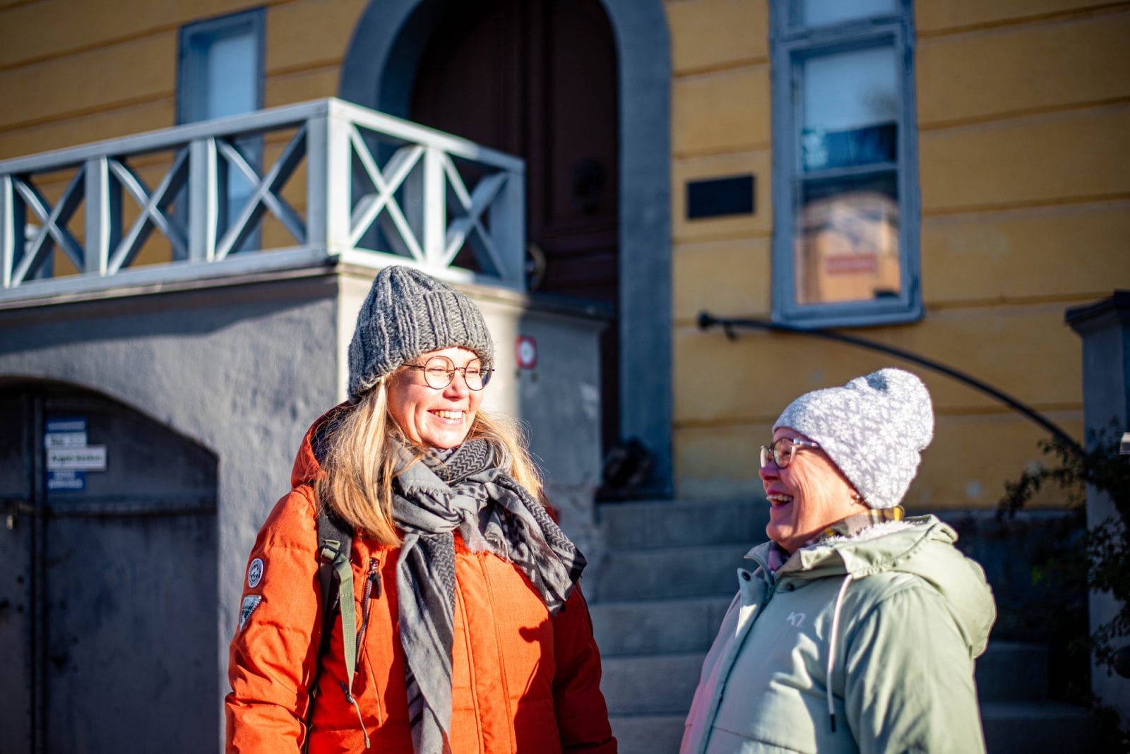 Kaksi pipopäistä naista nauraa keskenään auringon paistaessa museon rappusilla.