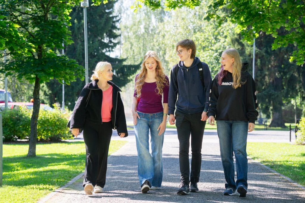 Neljä hymyilevää nuorta juttelee kävellen kesäisessä puistossa.