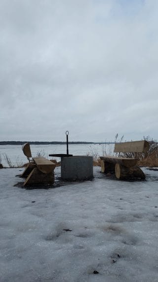 Nuotiopaikka talvimaisemassa. Nuotiopaikan ympärillä on kaksi penkkiä.