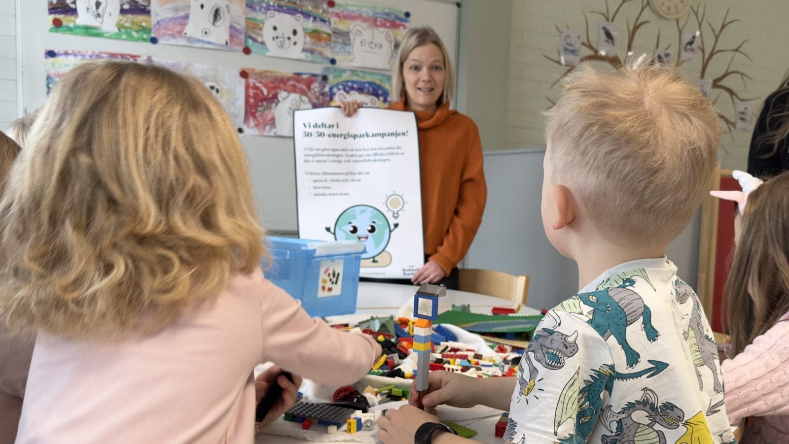 Nainen esittelee päiväkodin lapsille julistetta, joka kertoo energiansäästöstä.