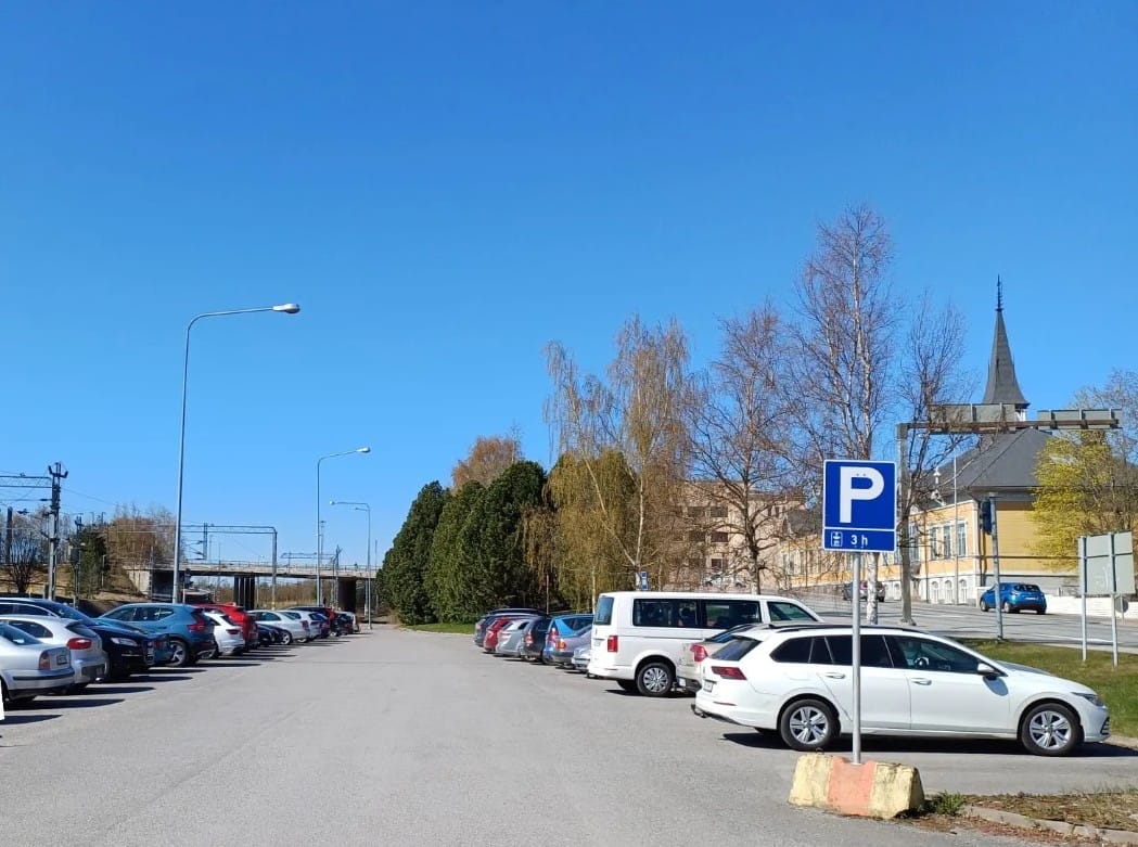 Pysäköintialue, jolla näkyy P-merkki ja autoja. Aurinko paistaa.