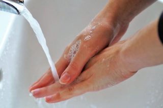 Käsiä pestään hanan alla, käsissä on saippuavaahtoa.
