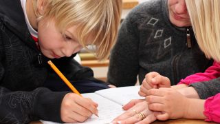 En pojke skriver för hand, en lärare handleder bredvid