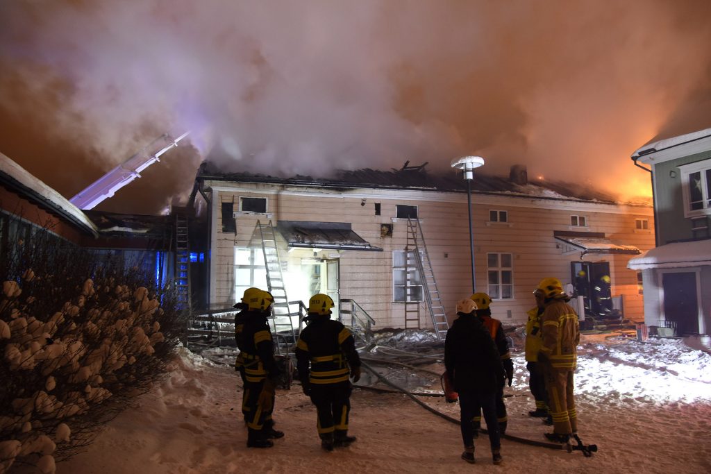 Räddningsverkets brandmän framför Kieppis brinnande timmerbyggnad.
