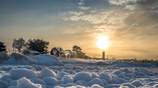Aurinko paistaa Harrbådan majakan takaa talvella.