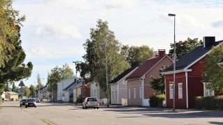 Gatuvy över Gustaf Adolfs gata. I bildens förgrund syns en tvåriktad väg med många bilar. I bildens högra kant bakom vägen syns frontmannahus i olika färger och på deras gårdar växer lövträd.