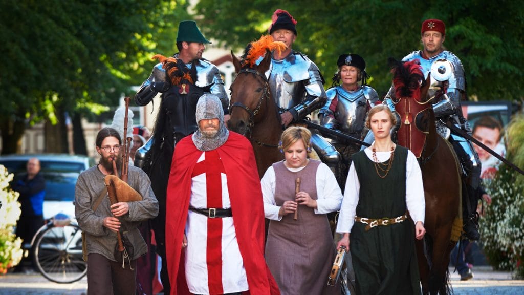 Joukko keskiaikaiseen asuun pukeutuneita ihmisiä ja hevosia astelee kohti