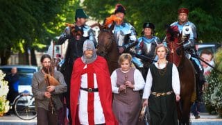 Joukko keskiaikaiseen asuun pukeutuneita ihmisiä ja hevosia astelee kohti