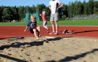 Kuvassa pieni lapsi urheilukentällä hyppäämässä pituutta