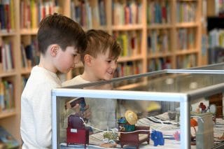Two young boys look at a glass case display with doll house items.