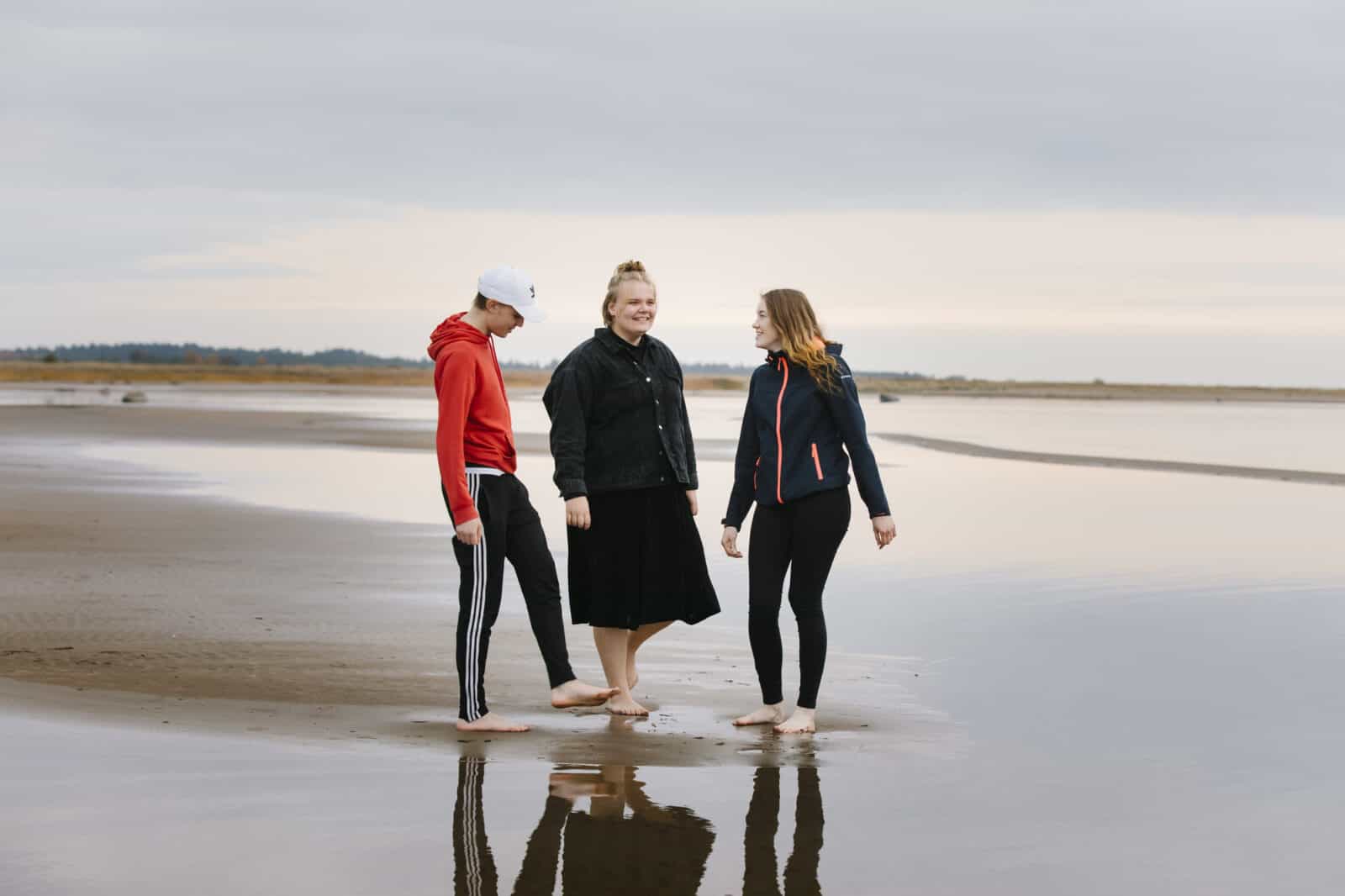 Kolme nuorta seisoo rannalla nousuveden aikaan